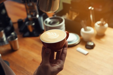 Photo of Barista holding cup of coffee at bar counter, closeup. Space for text