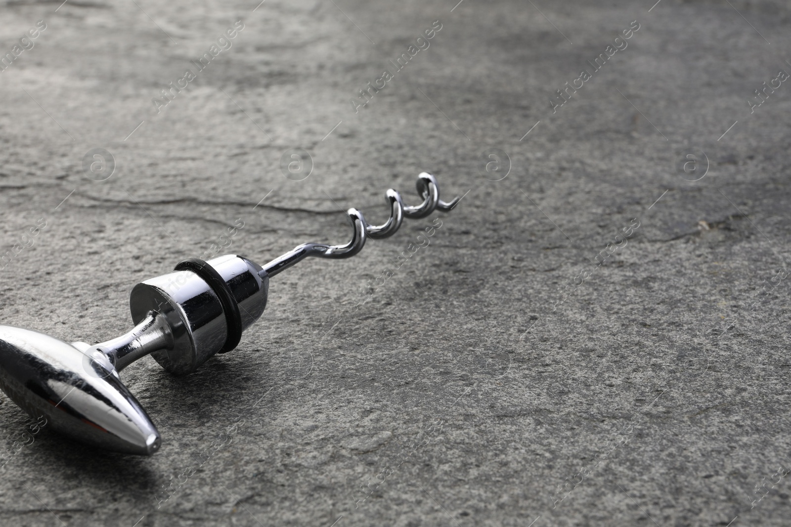 Photo of One metal corkscrew on grey textured table, closeup. Space for text