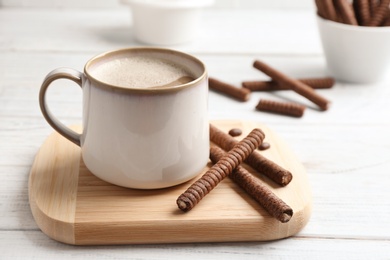 Delicious chocolate wafer rolls and cup of coffee on wooden table. Space for text