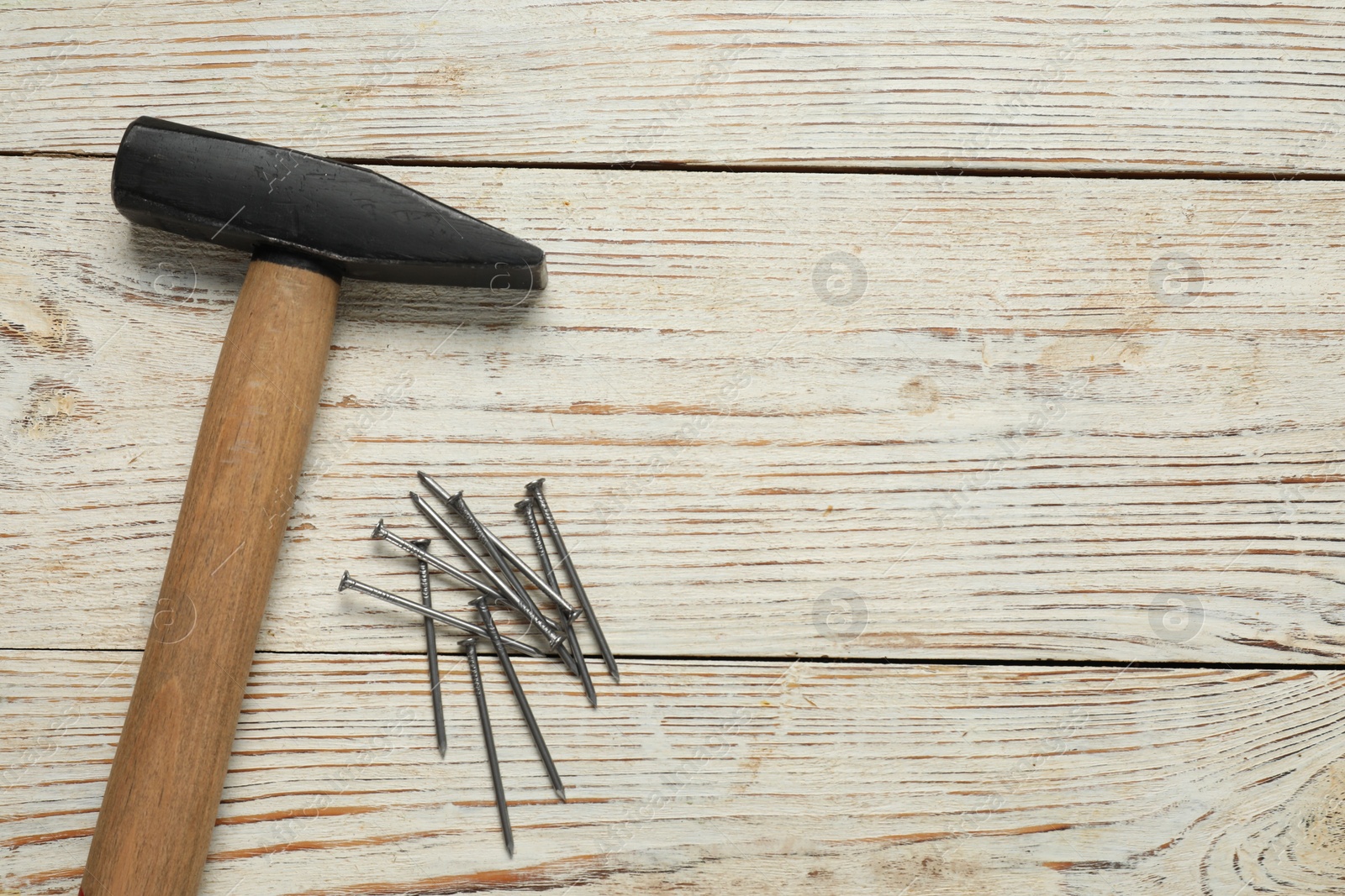 Photo of New hammer and metal nails on wooden table, flat lay. Space for text