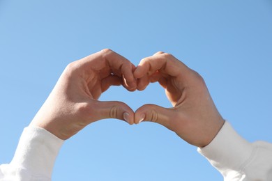 Photo of Man showing heart against blue sky outdoors on sunny day, closeup of hands