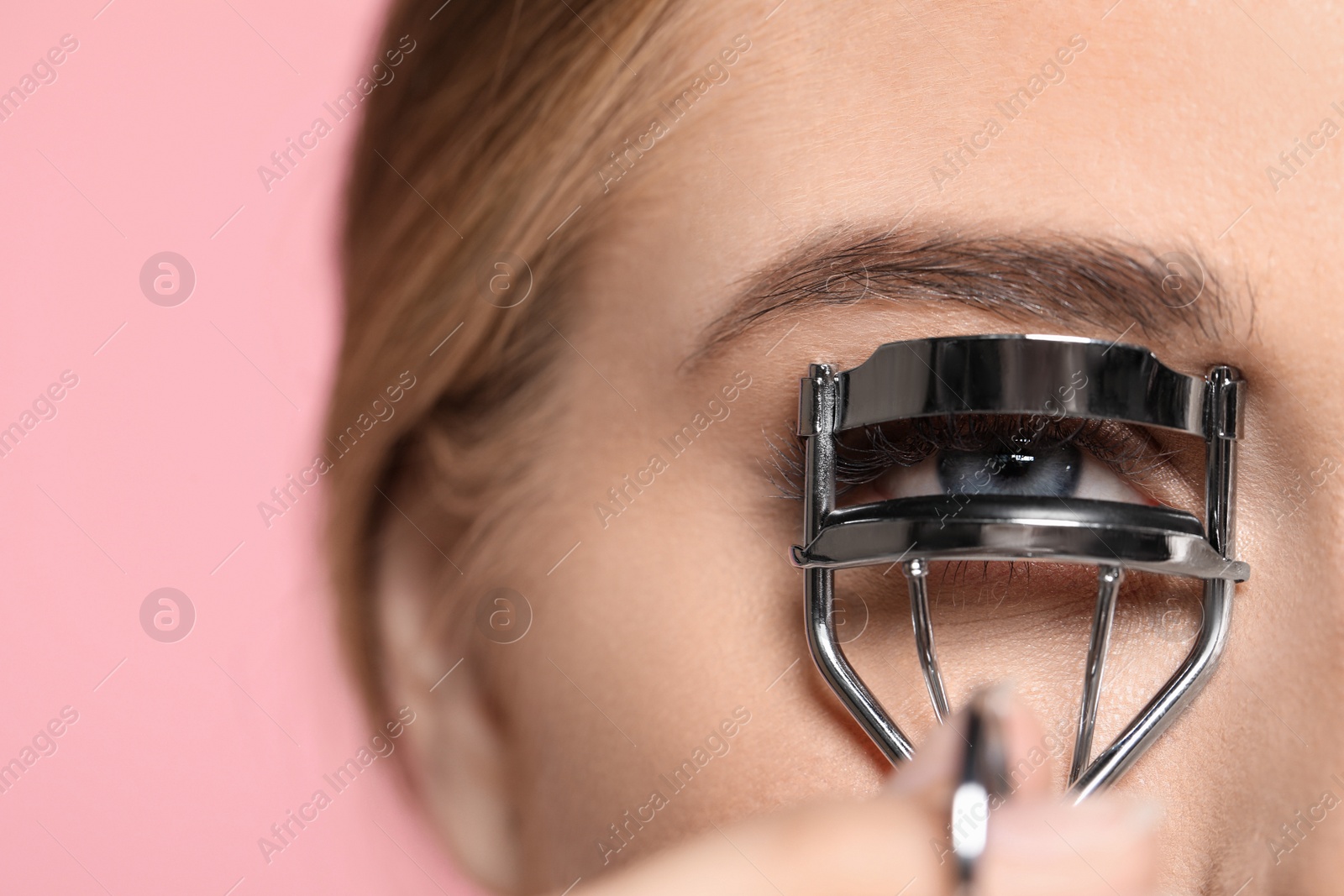 Photo of Young woman using eyelash curler on pink background, closeup