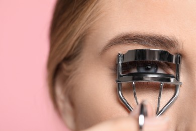 Young woman using eyelash curler on pink background, closeup