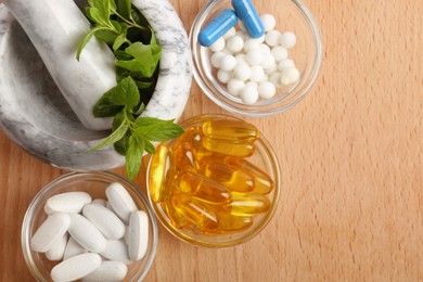 Mortar with fresh mint and pills in bowls on wooden table