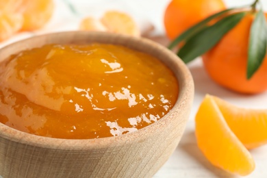 Photo of Tasty tangerine jam in wooden bowl on white table, closeup