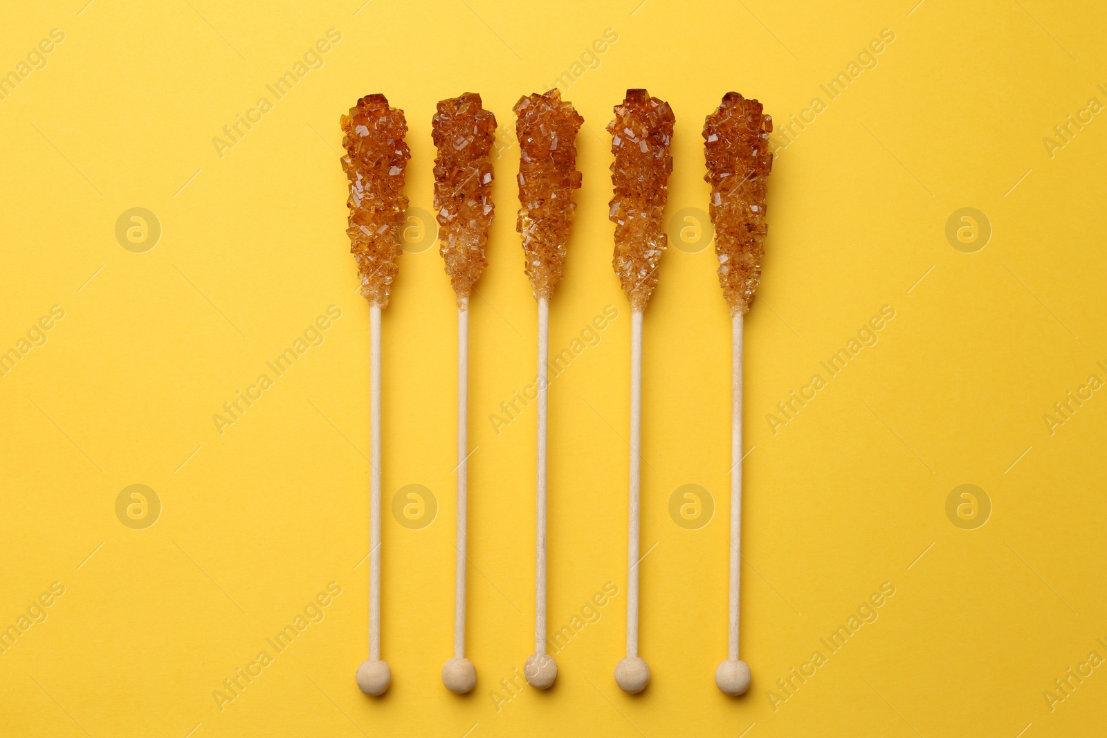 Photo of Wooden sticks with sugar crystals on yellow background, flat lay. Tasty rock candies