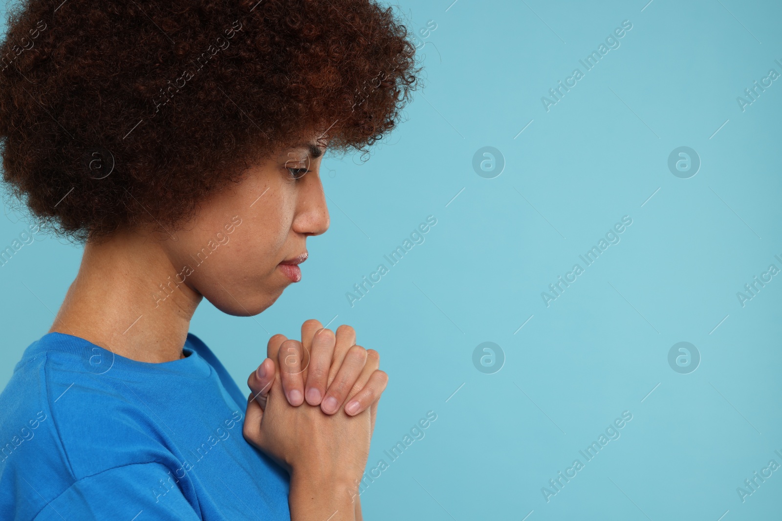 Photo of Woman with clasped hands praying to God on light blue background. Space for text