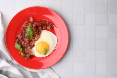 Fried egg, bacon and basil on white tiled table, top view. Space for text