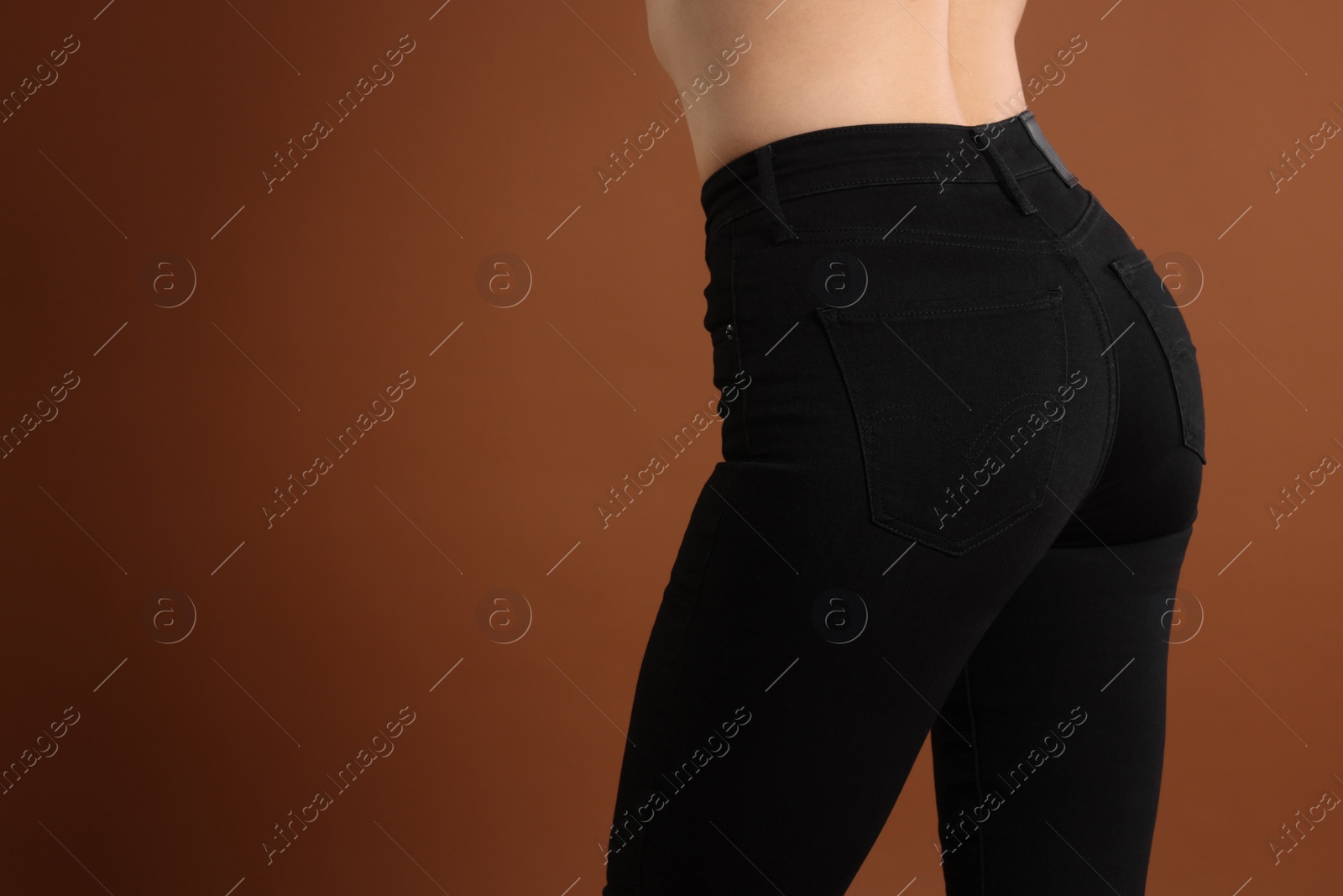 Photo of Woman wearing stylish black jeans on brown background, closeup. Space for text