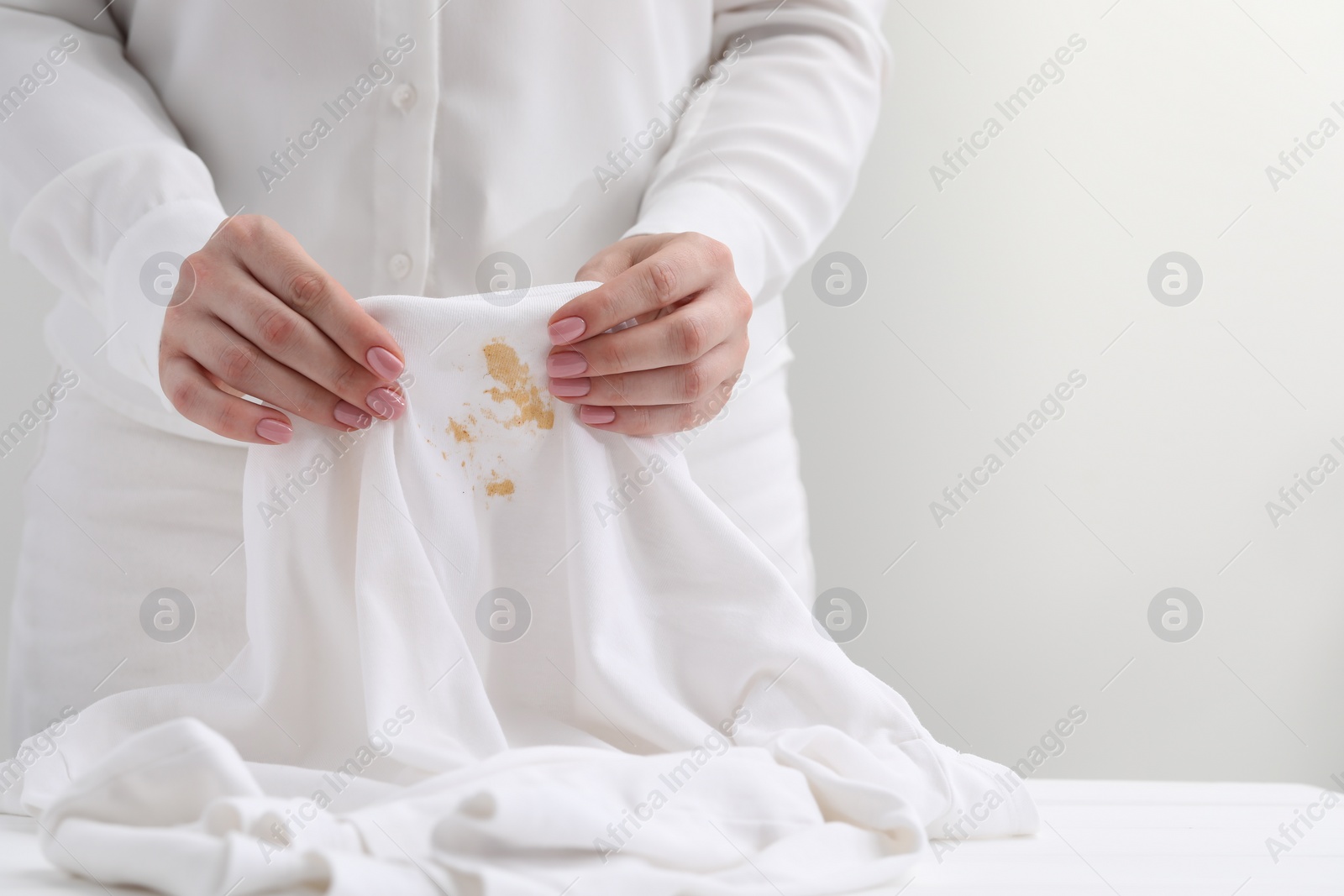 Photo of Woman holding shirt with stain at table against light background, closeup. Space for text