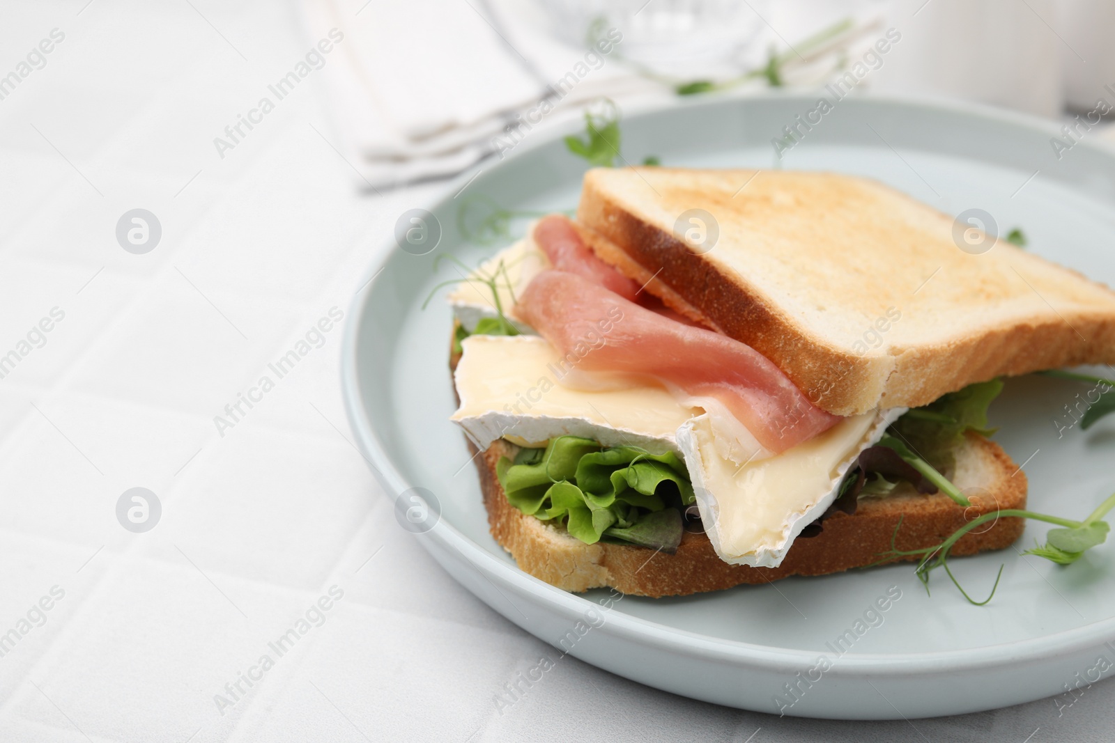 Photo of Tasty sandwich with brie cheese and prosciutto on white tiled table, closeup. Space for text