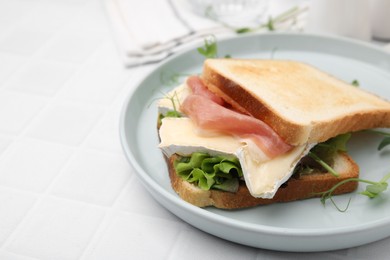 Tasty sandwich with brie cheese and prosciutto on white tiled table, closeup. Space for text