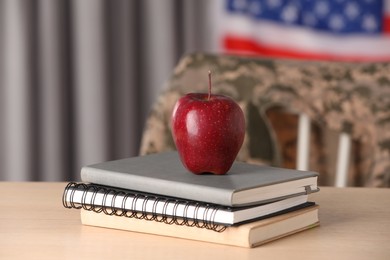 Photo of Notebooks and apple on wooden table near flag of United States indoors. Military education