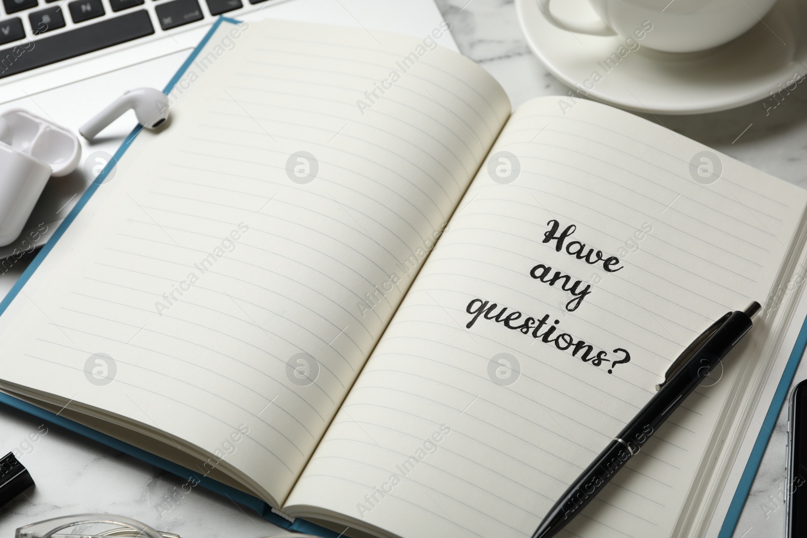 Photo of Notebook with phrase HAVE ANY QUESTIONS on white marble table, closeup