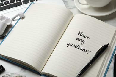 Photo of Notebook with phrase HAVE ANY QUESTIONS on white marble table, closeup