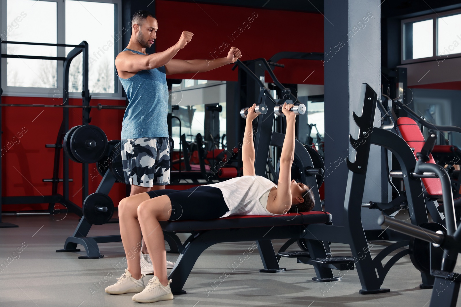 Photo of Young woman working out with professional trainer in modern gym