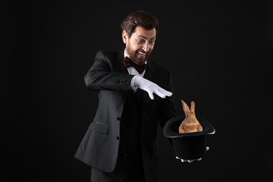 Magician showing trick with top hat and rabbit on black background