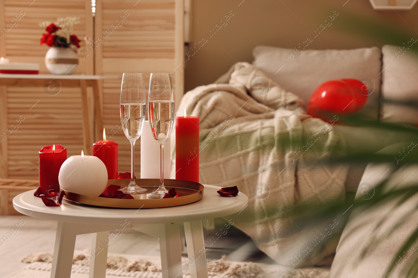 Photo of Glasses of sparkling wine, candles and petals on white table indoors. happy Valentine's Day