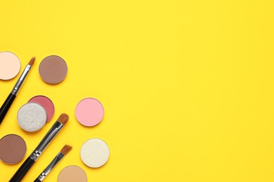 Photo of Beautiful eye shadow refill pans and makeup brushes on yellow background, flat lay. Space for text