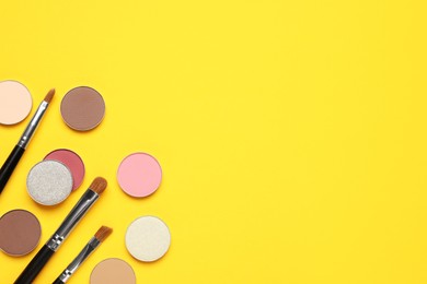 Beautiful eye shadow refill pans and makeup brushes on yellow background, flat lay. Space for text