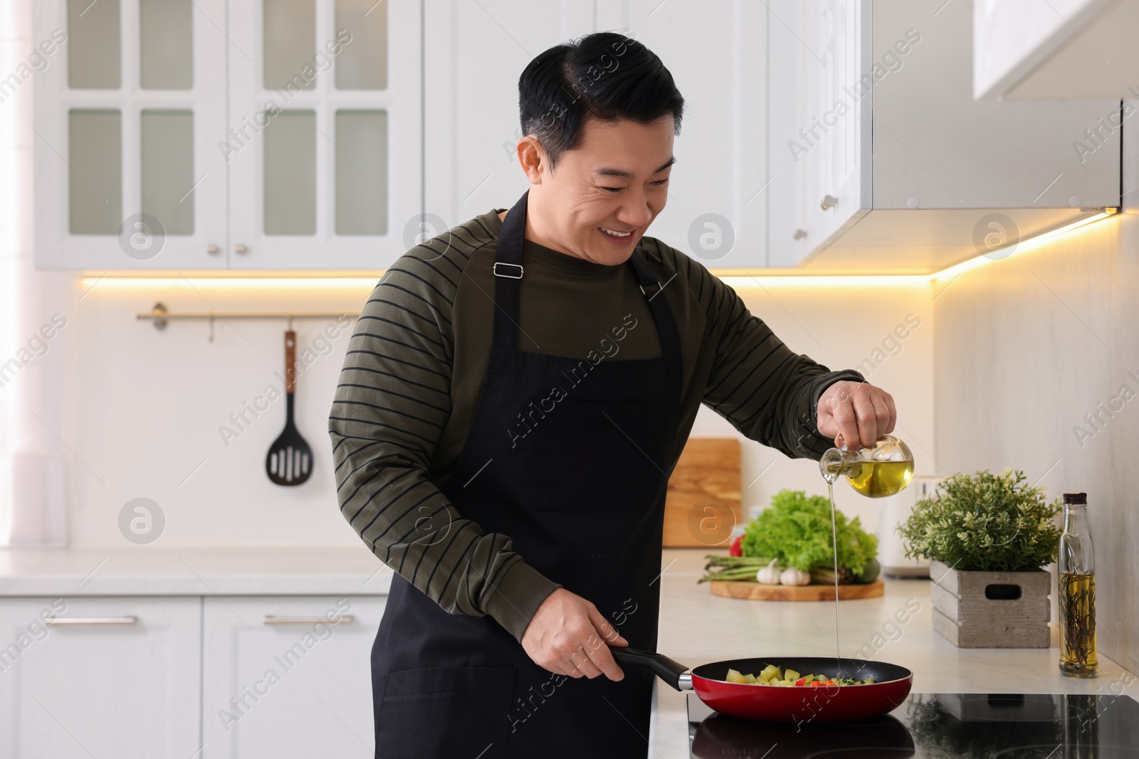 Photo of Cooking process. Happy man pouring oil into frying pan in kitchen, space for text