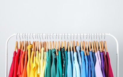 Photo of Rack with bright clothes on light blue background. Rainbow colors