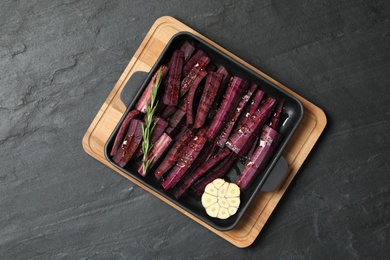 Photo of Black raw cut carrot with garlic and rosemary in baking dish on black slate table, top view