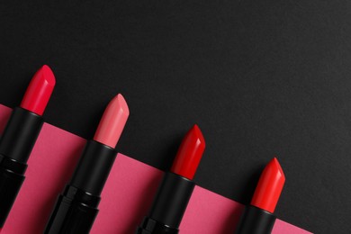 Photo of Beautiful lipsticks on black and pink background, flat lay. Space for text