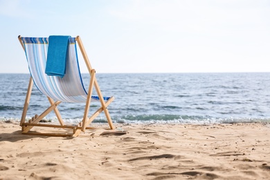 Photo of Lounger and towel on sand near sea, space for text. Beach objects