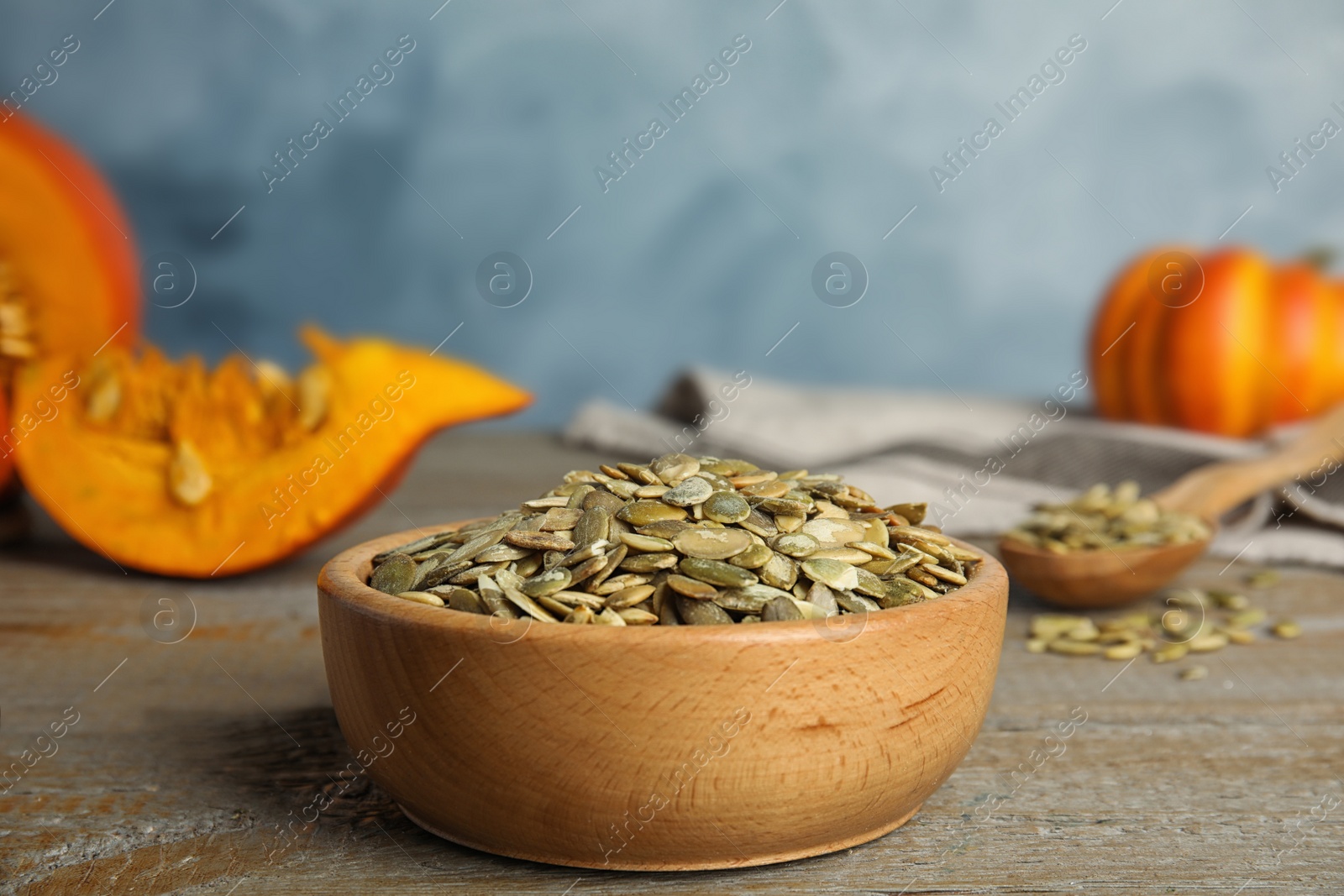 Photo of Bowl of raw peeled pumpkin seeds on wooden table against blue background. Space for text