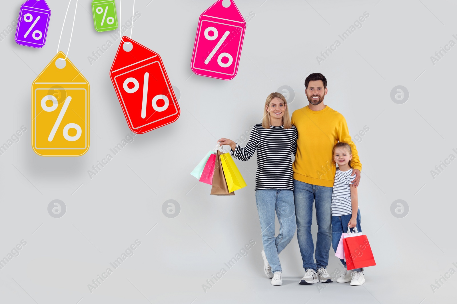 Image of Discount offer. Happy family with paper shopping bags on light grey background. Labels with percent signs hanging near them