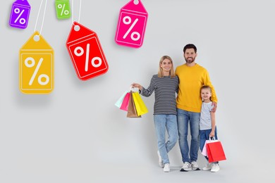 Image of Discount offer. Happy family with paper shopping bags on light grey background. Labels with percent signs hanging near them