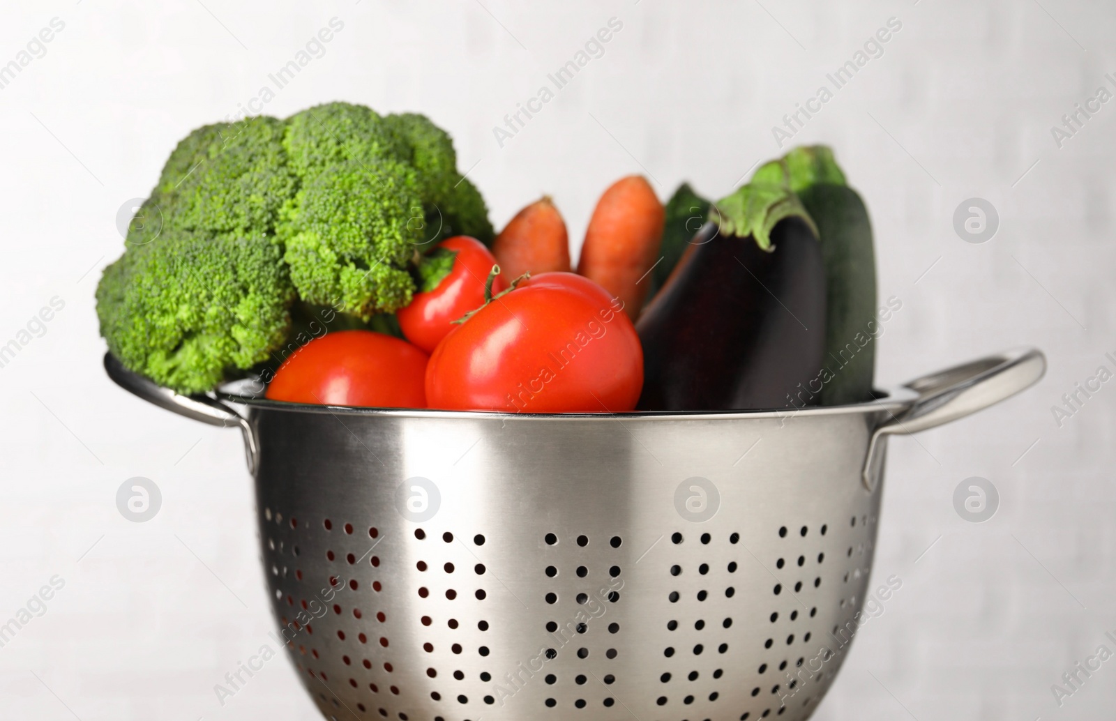 Photo of Fresh vegetables in colander on light background, closeup