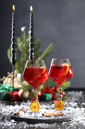Photo of Christmas Sangria cocktail in glasses, burning candles and snow on dark wooden table