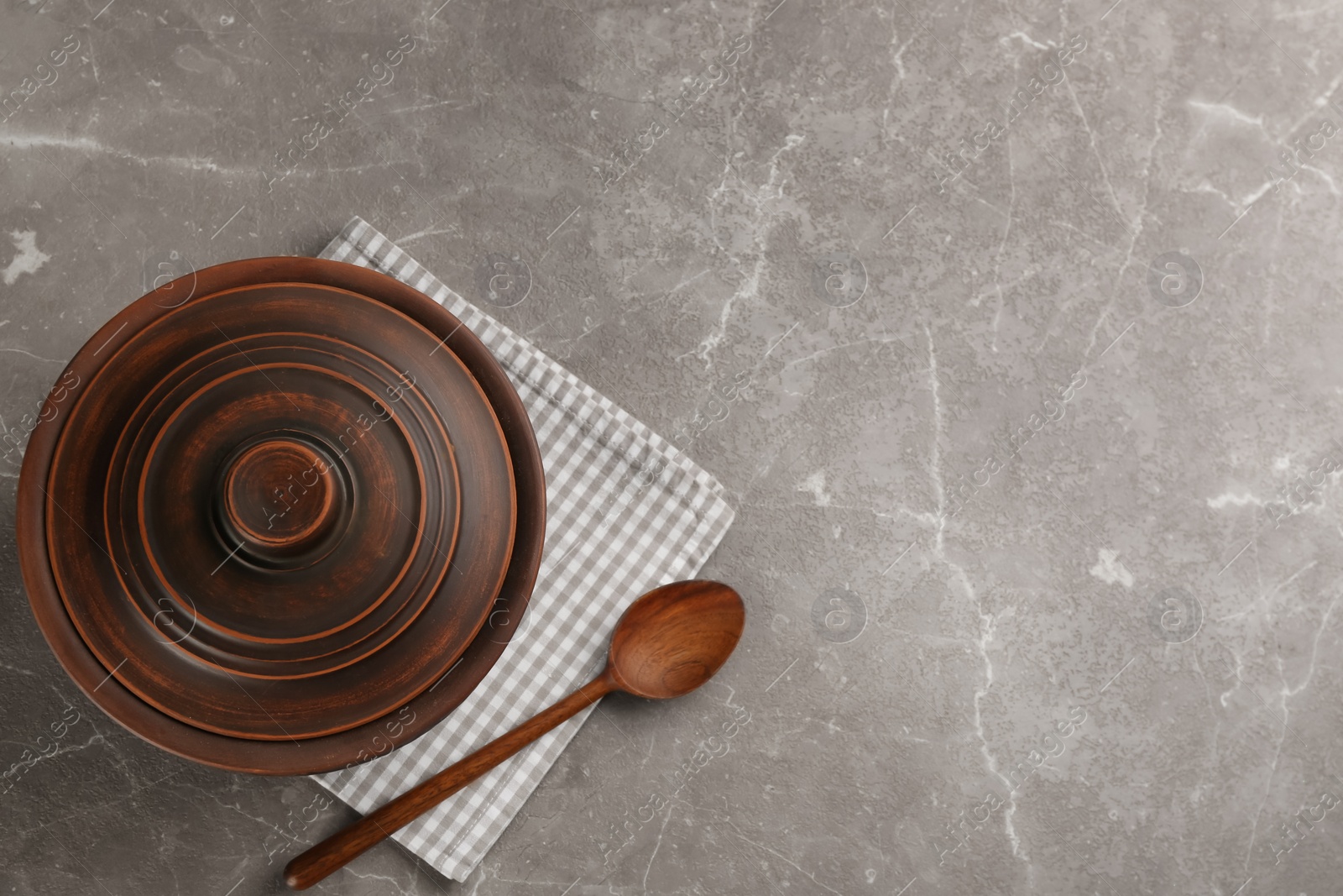 Photo of Clay pot, spoon and towel on grey marble table, flat lay with space for text. Handmade utensils