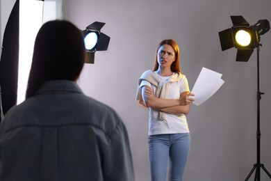 Emotional woman with script performing in front of casting director against grey background at studio