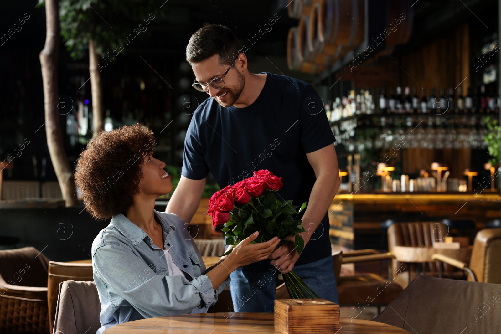 Photo of International relationships. Handsome man presenting roses to his beloved woman in cafe