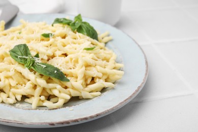 Plate of delicious trofie pasta with cheese and basil leaves on white tiled table, closeup. Space for text