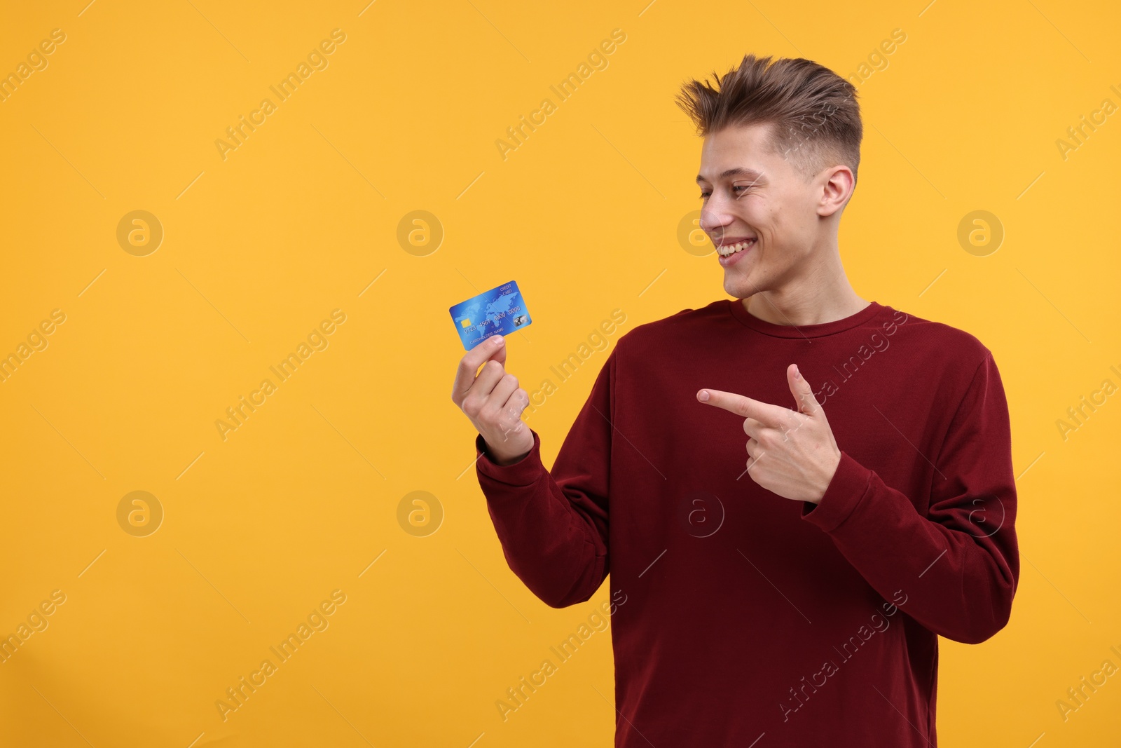 Photo of Happy man pointing at credit card on yellow background. Space for text