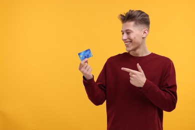 Happy man pointing at credit card on yellow background. Space for text