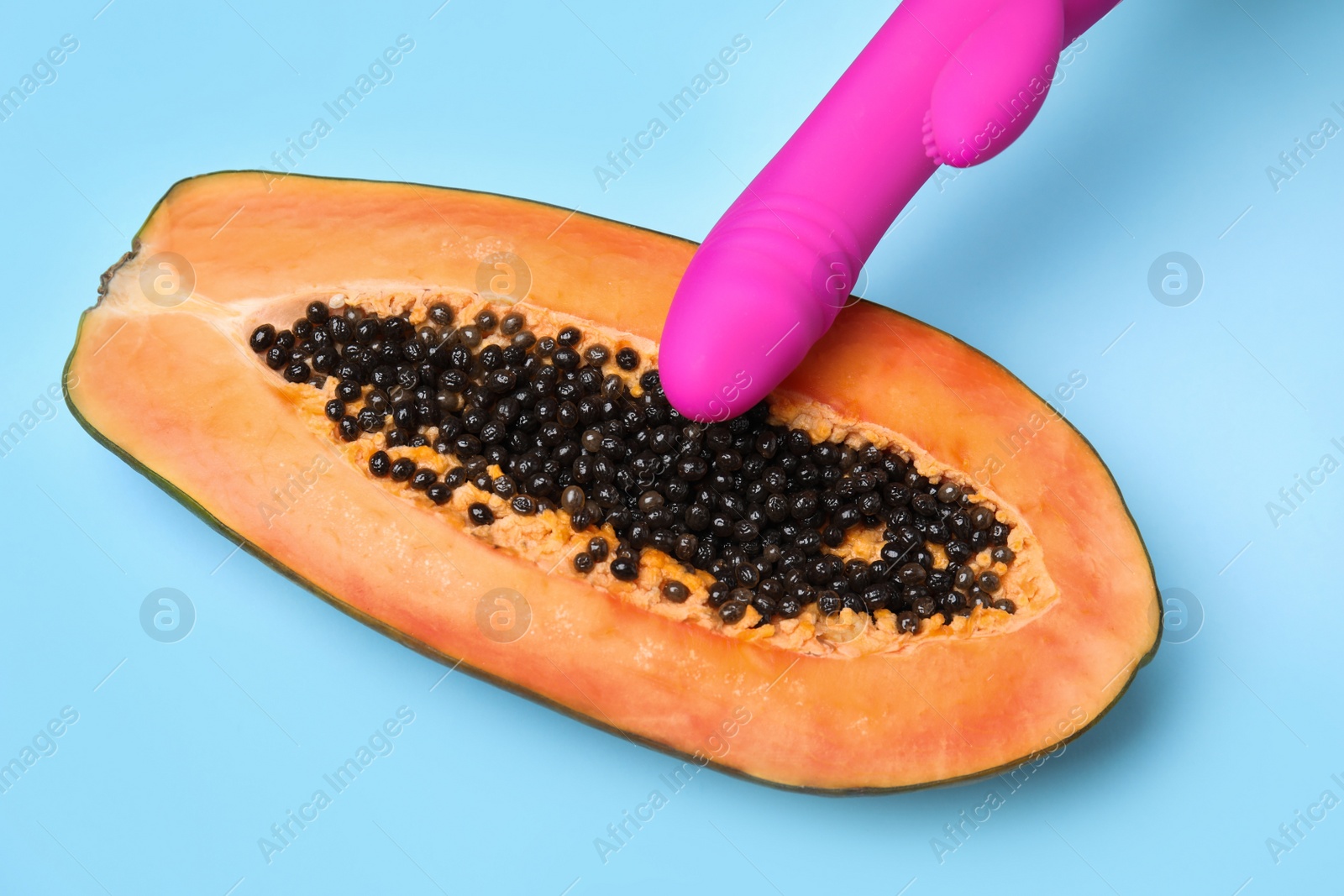 Photo of Half of papaya and purple vibrator on blue background, top view. Sex concept