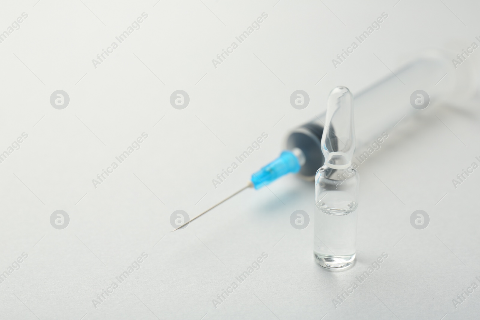 Photo of Glass ampoule with liquid and syringe on white background, closeup. Space for text