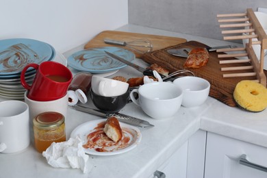 Many dirty utensils, dishware and food leftovers on countertop in messy kitchen