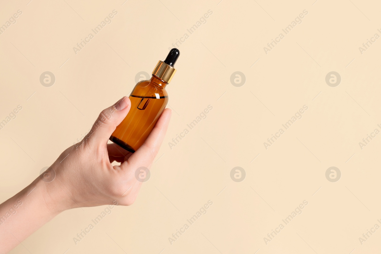 Photo of Woman holding bottle of cosmetic oil on beige background, closeup. Space for text