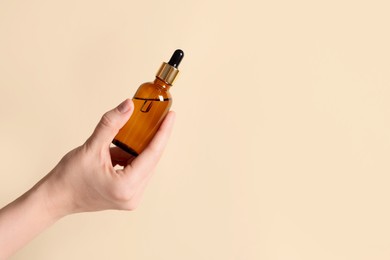 Photo of Woman holding bottle of cosmetic oil on beige background, closeup. Space for text