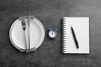 Business lunch concept. Plates, cutlery, alarm clock, notebook and pen on gray textured background, flat lay