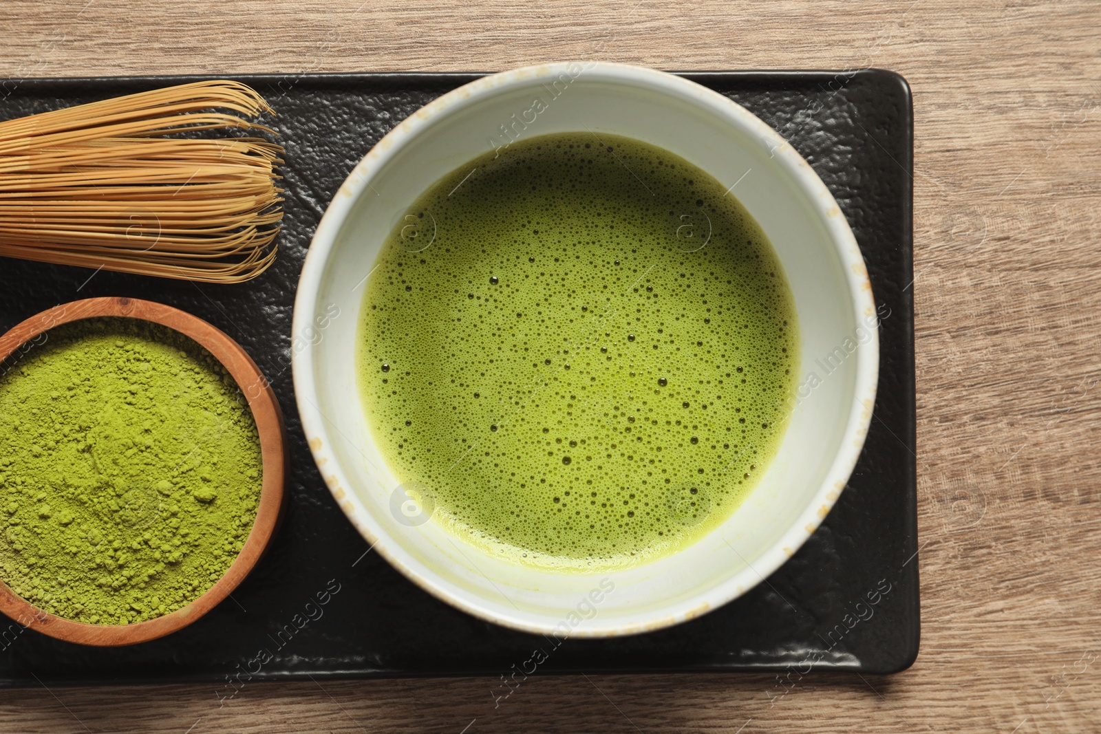 Photo of Cup of fresh matcha tea, bamboo whisk and green powder on wooden table, top view