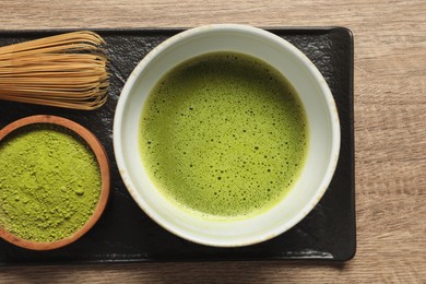 Cup of fresh matcha tea, bamboo whisk and green powder on wooden table, top view