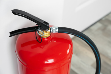 Photo of Fire extinguisher near white wall indoors, closeup 