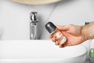 Photo of Man holding roll-on deodorant in bathroom, closeup
